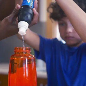 Screenshot from video of child and adult using personal water filter to direct potable water into a bottle